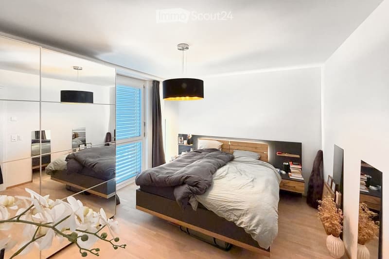 Modern bedroom with a large bed, nightstand, mirror, pendant light, and decorative vases.