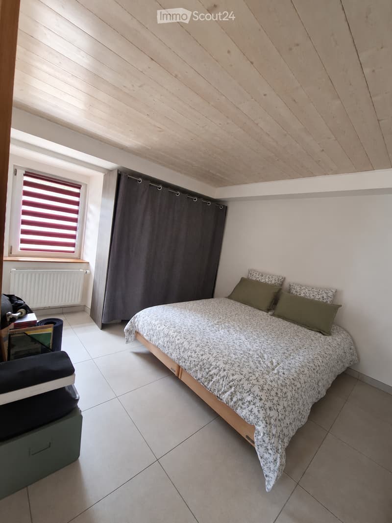 Cozy bedroom with a single bed, green pillows, a window with red and black blinds, a radiator, and a storage box.