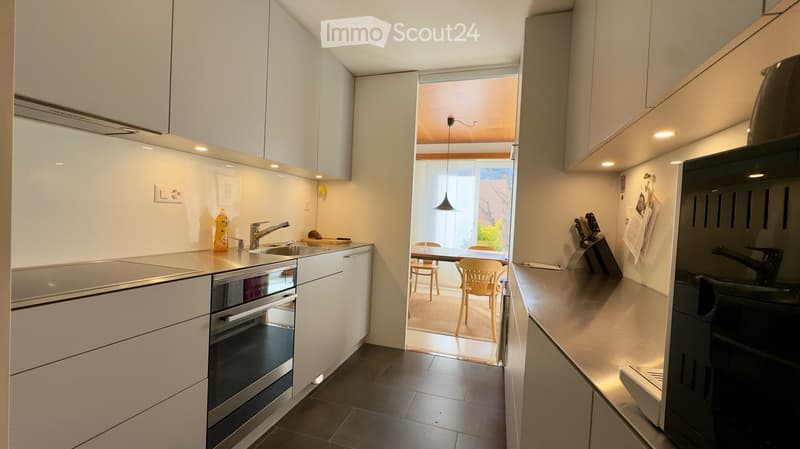 Modern kitchen with white cabinets, stainless steel appliances, and a view into a dining area with a table and chairs.