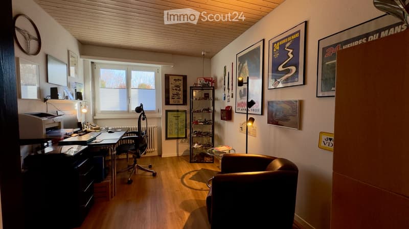 A well-lit room with wooden flooring, a desk setup, a leather armchair, and several framed pictures and posters on the walls.
