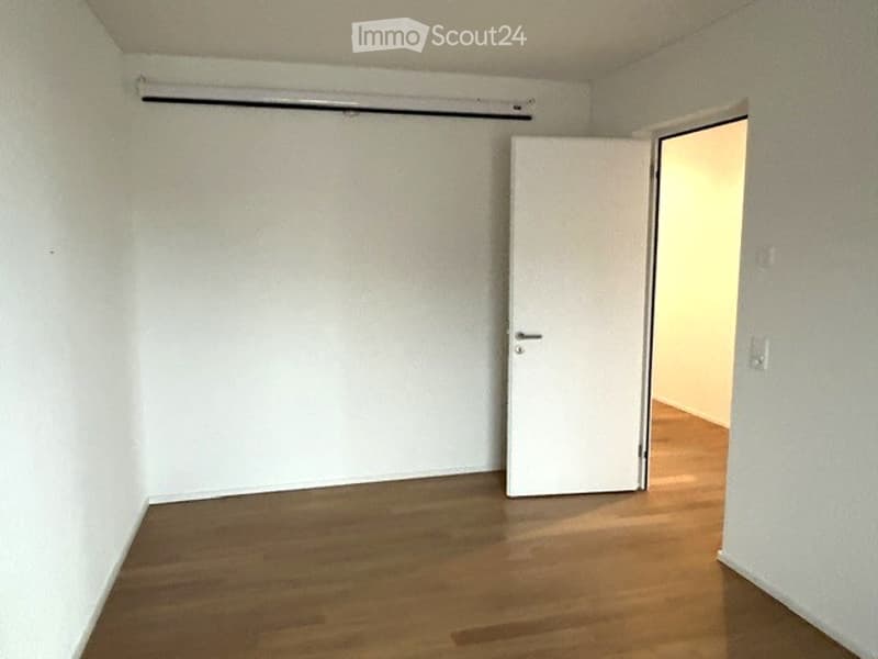 Empty room with wooden flooring, white walls, and a single door leading to another space.