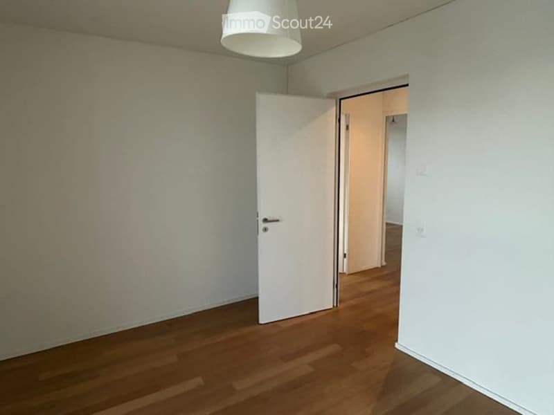 Empty room with wooden flooring, white walls, and a single open door leading to another room.