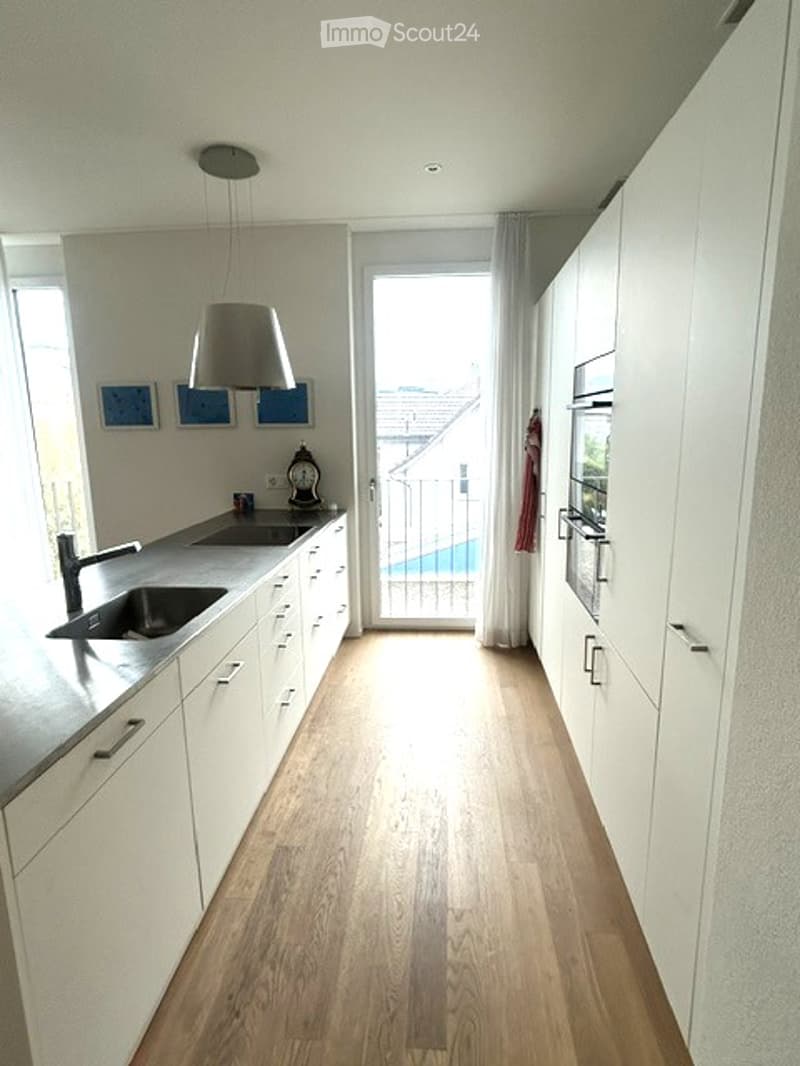 Modern kitchen with white cabinets, stainless steel sink, and a view of a swimming pool through the glass door.