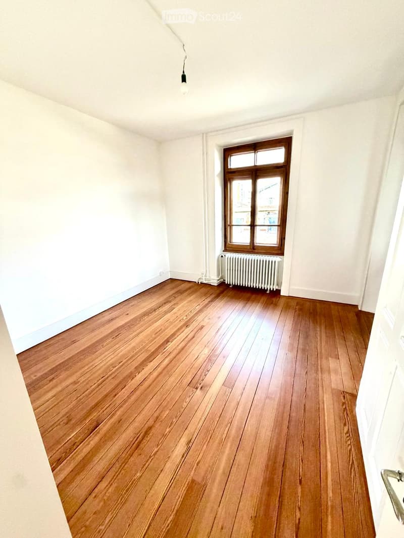 Empty room with wooden flooring, white walls, a single window with wooden frame, and a radiator below the window.