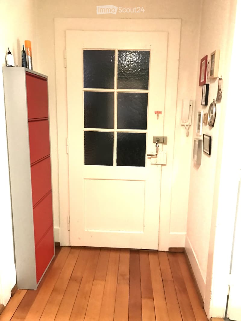 narrow hallway with wooden floor, white door, grey and red cabinet, wall mounted frames