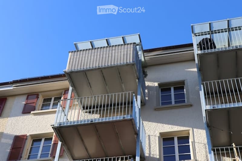 white stucco building, multiple balconies with railings, wooden shutters on windows
