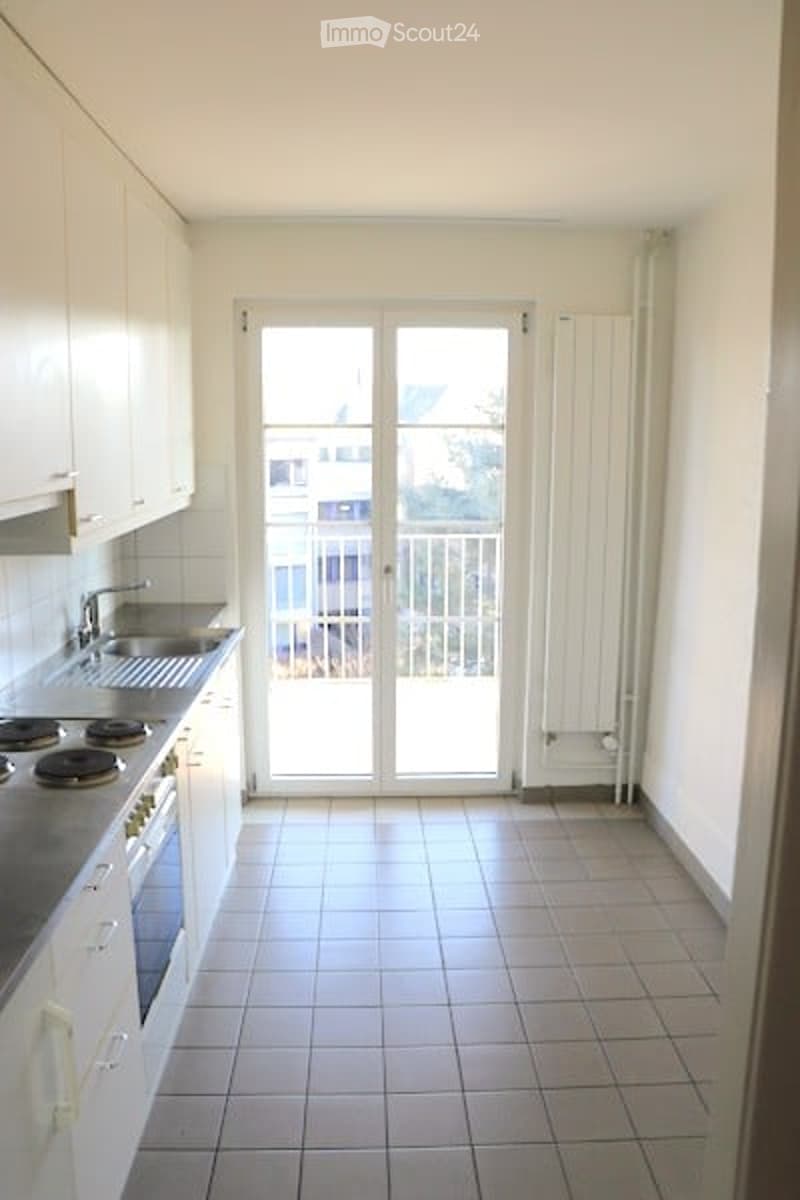 white cabinets, black granite countertops, gas stove, dishwasher, white tiled flooring, large window with sliding door leading to balcony