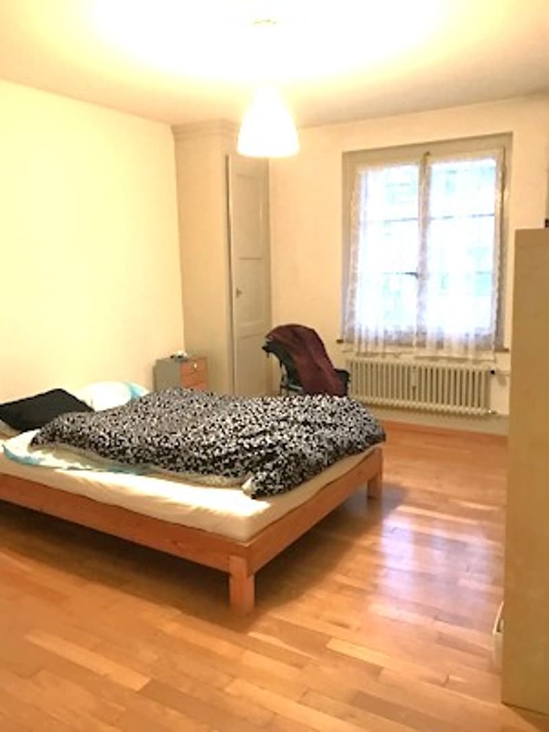 small bedroom with bed, wooden floor, large window, wardrobe, radiator