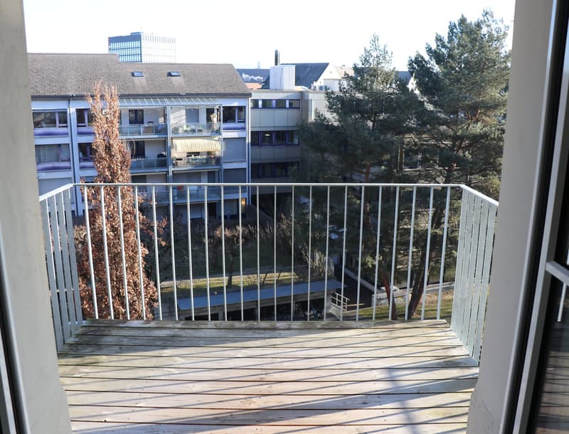 Wooden balcony with railings, overlooking buildings and trees