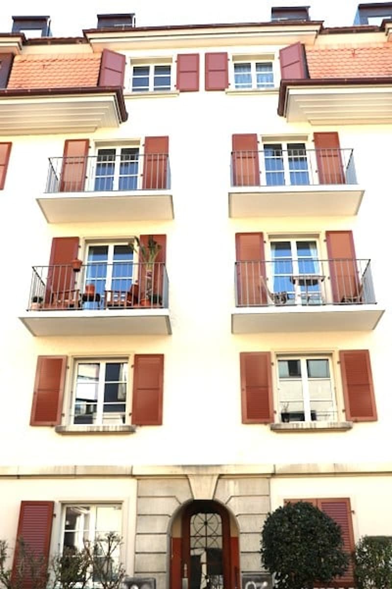 3 story building, white exterior, red shutters, balconies with tables, chairs and potted plants