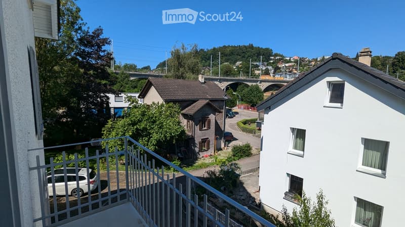 Balcony overlooking a residential area with houses, trees, and a bridge in the background.