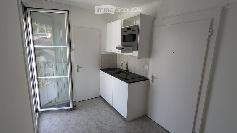 Modern kitchen with white cabinets, black countertop, sink, faucet, and microwave. Features a large window and a door leading outside.