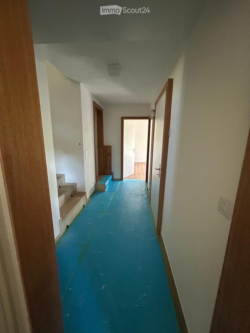 Empty hallway with blue flooring, white walls, and wooden doors leading to other rooms.