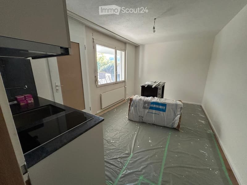 Empty room with bare walls, a window, a door, and a covered appliance. The floor is covered with protective plastic sheeting.