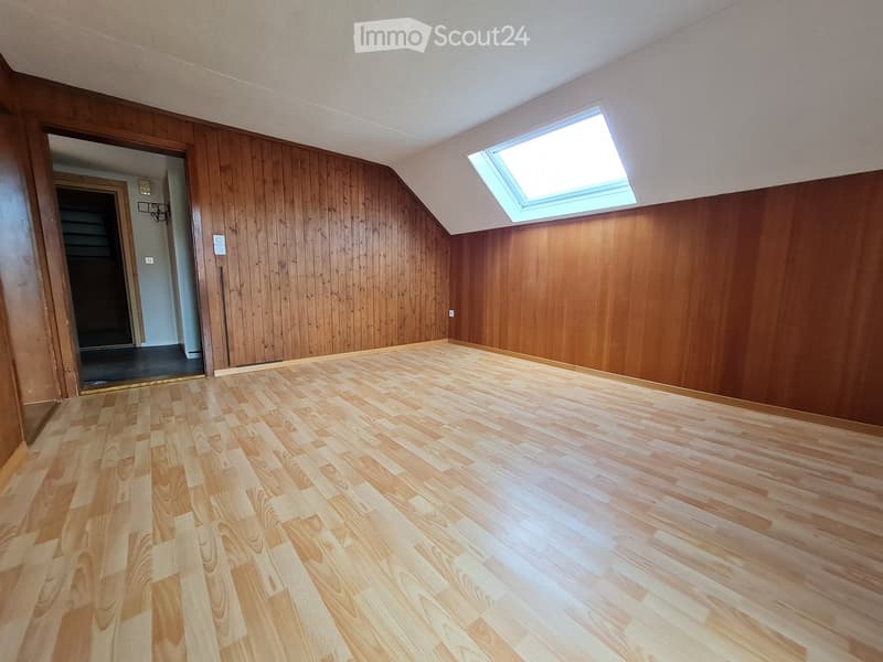 Empty room with wooden walls and flooring, featuring a skylight window and an open doorway leading to a staircase.