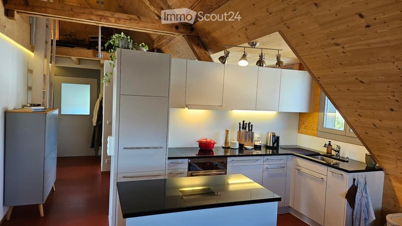 Modern kitchen with white cabinets, stainless steel appliances, and wooden beams on the ceiling. Features include a central island, built-in oven, and various kitchen utensils.