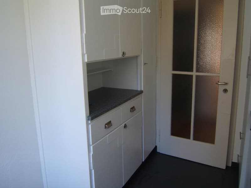 Empty room with white cabinets, a countertop, and a door with frosted glass panels.