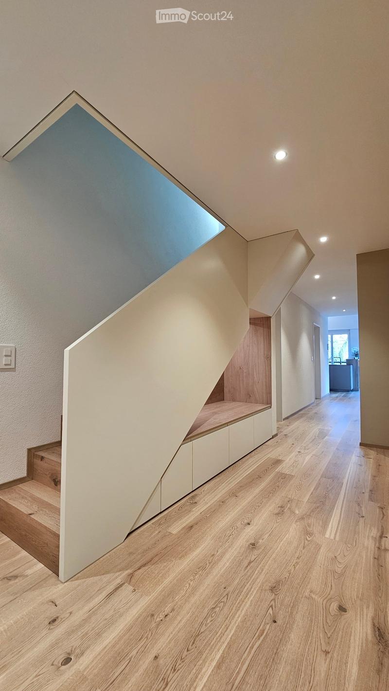 A modern staircase with wooden steps and white wall, built-in wooden bench underneath, and a ceiling with built-in skylights