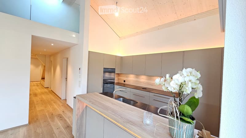 Contemporary kitchen with wooden floors, sleek gray cabinetry, a wooden countertop, stainless steel sink, white flowers in a blue pot, and a modern lighting fixture.