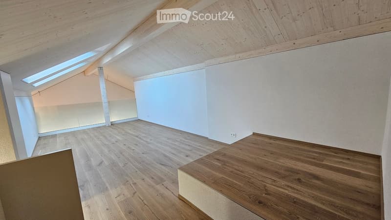 A room with wooden floor, white walls, wooden beams on the ceiling and skylight windows