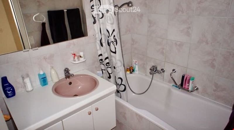 Bathroom with a pink sink, white countertop, mirror, bathtub, and shower curtain. Various toiletries and a towel are visible.