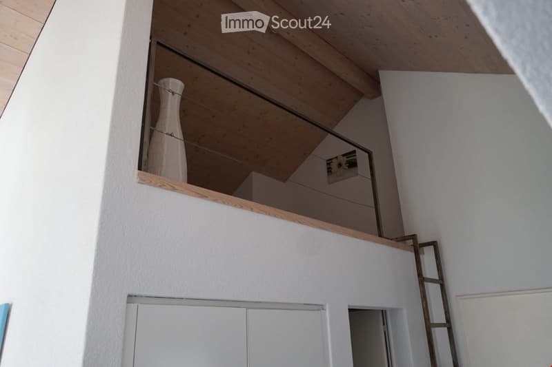 A modern, minimalist hallway with white walls, wooden ceiling beams, and a small shelf holding a white vase. The space features clean lines and a contemporary design.