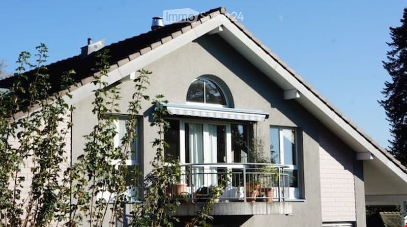 Modern two-story house with a grey exterior, large windows, and a balcony with potted plants.