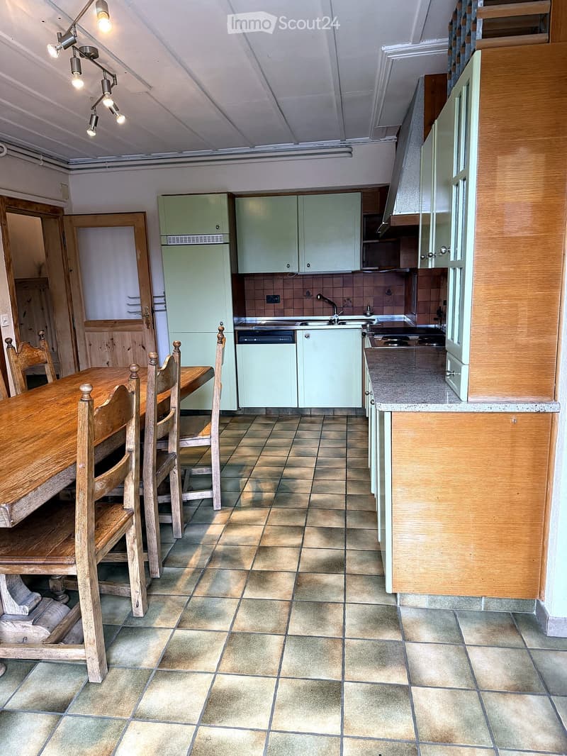 A kitchen with tiled flooring, wooden dining table and chairs, light green cabinets, a refrigerator, dishwasher, sink, and faucet.