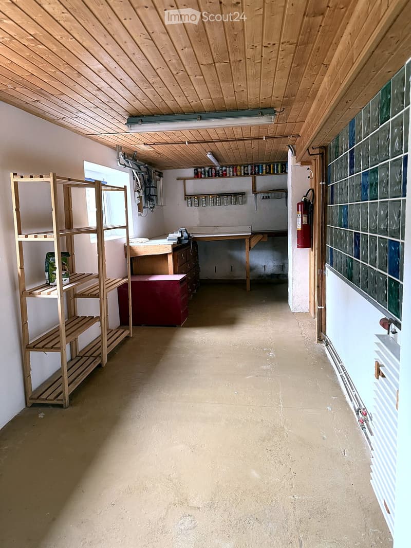 Empty attic or storage space with wooden beams, concrete floor, shelves, and a workbench.