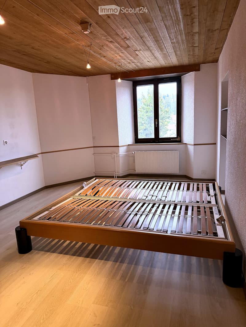 Spacious bedroom with wooden floor, large window, and a wooden bed frame with slats.