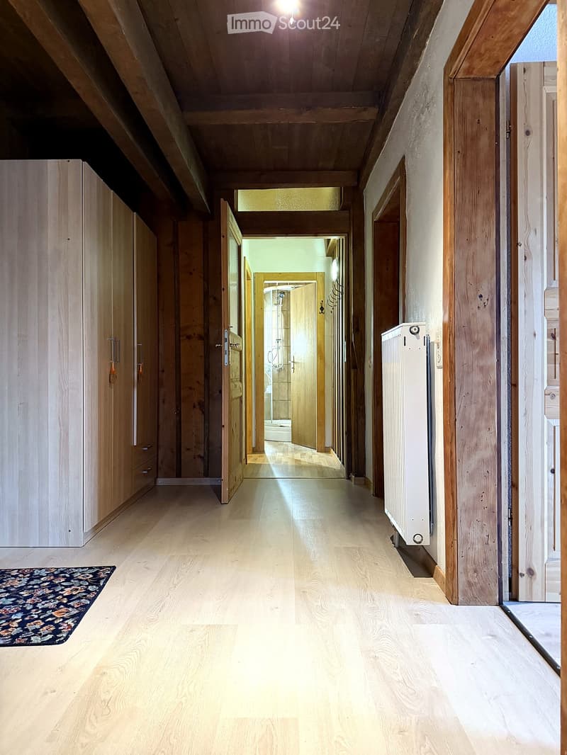Spacious hallway with wooden flooring, wooden doors, and a radiator on the right side. A small rug is placed on the left side of the hallway.
