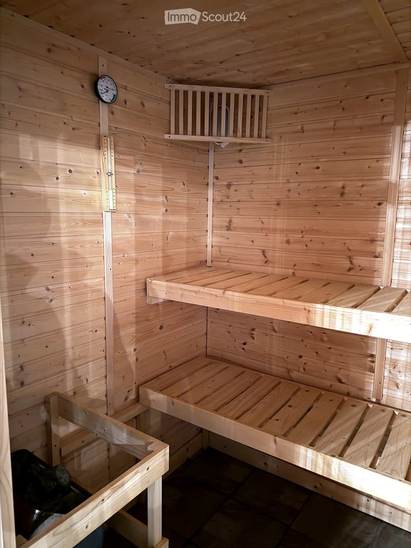 Wooden sauna interior with built-in benches and shelves, featuring a thermometer on the wall.