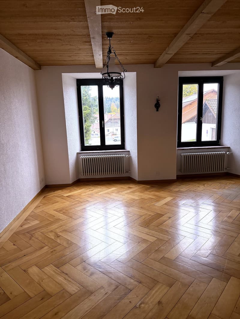 Empty room with wooden herringbone flooring, large windows, radiators, and a chandelier fixture.