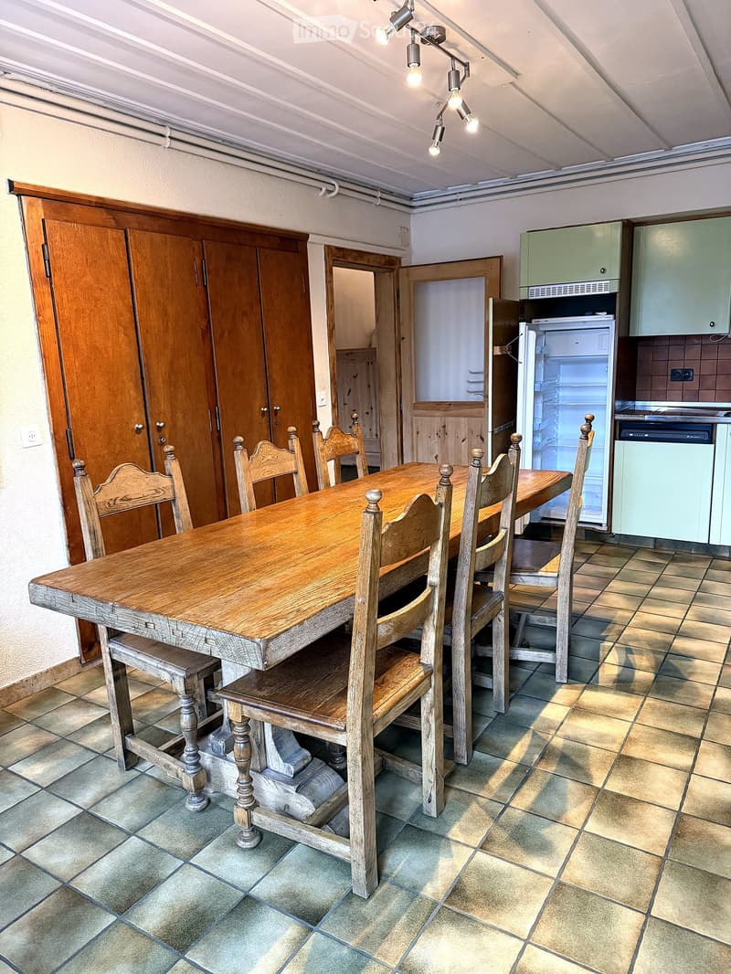 Dining area with a wooden dining table and chairs, a refrigerator, and cabinets.
