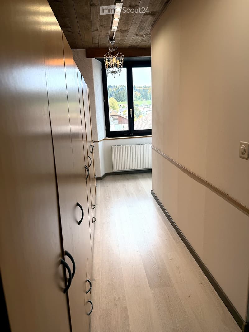 Modern hallway with light wooden flooring, built-in wardrobes, a chandelier, and a large window offering a view of the outdoors.