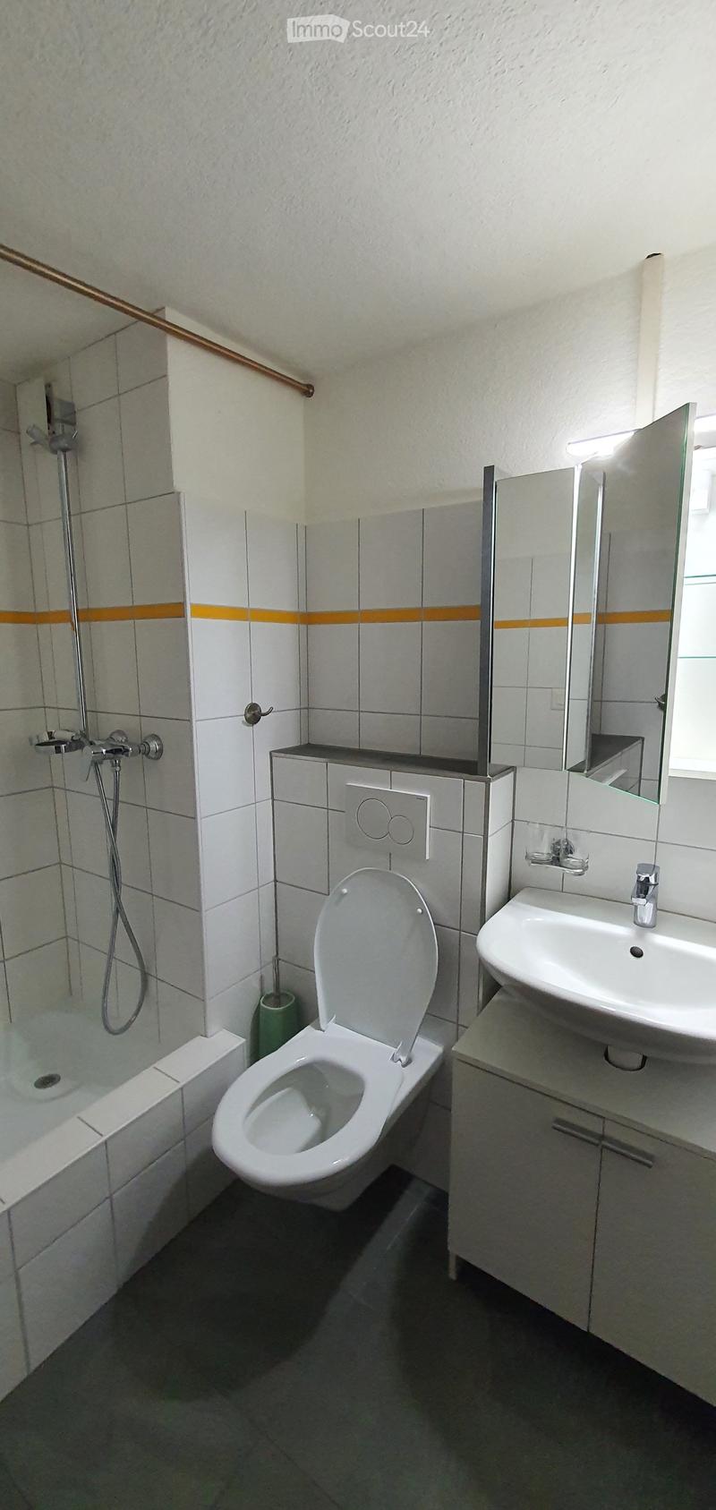 Modern bathroom with white tiles, a toilet, a sink with a mirror, a bathtub, and a shower area with a glass enclosure.