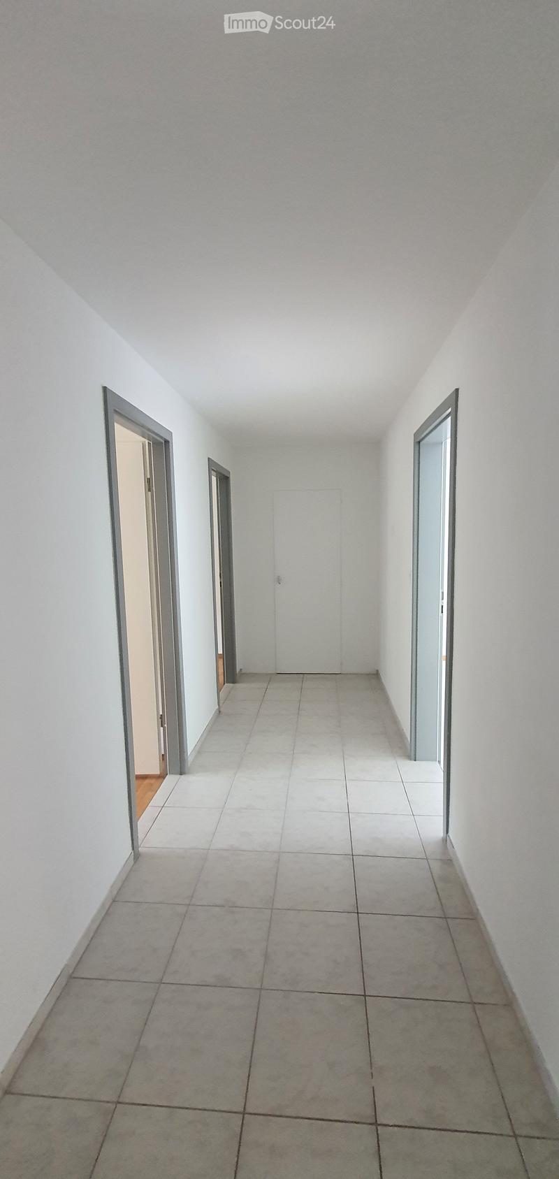 Empty hallway with tiled floor, white walls, and three doors leading to other rooms.