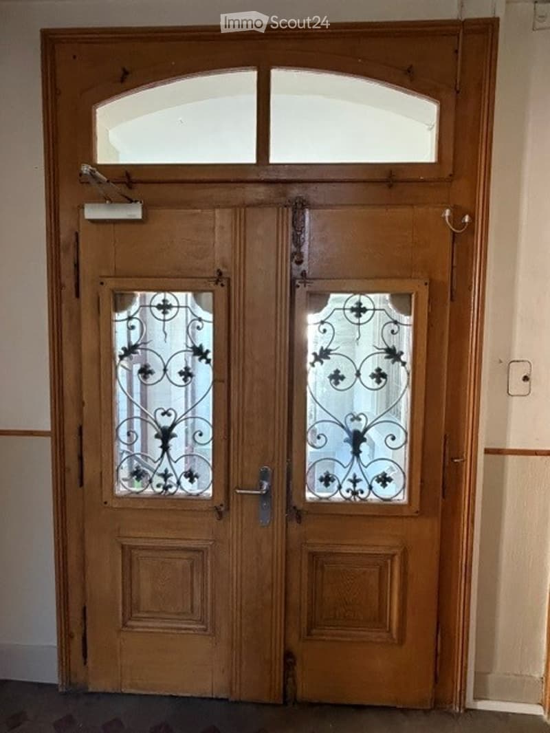 Double wooden door with decorative glass panels and ornate metalwork, featuring a transom window above.