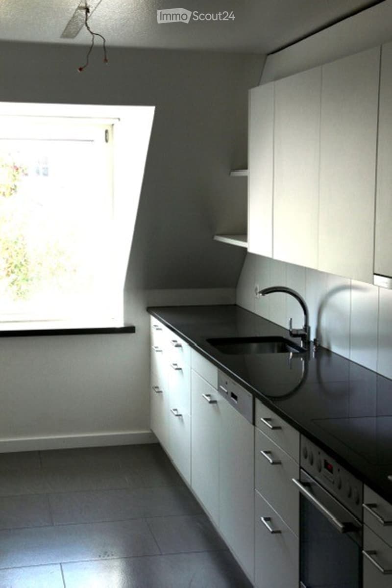 Modern kitchen with white cabinets, black countertops, and a stainless steel sink. The space features built-in storage and a large window providing natural light.