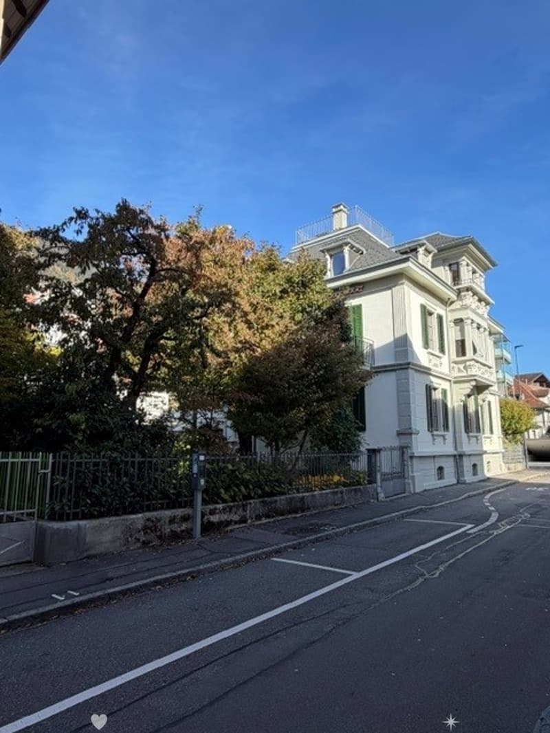 A multi-story residential building with classic architecture, white facade, green shutters, and a small balcony on the roof.