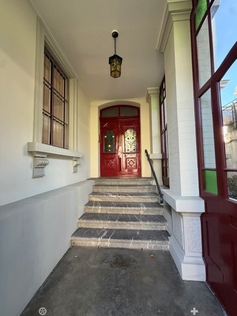 Raised entranceway with a staircase leading up to a red double door, flanked by white walls and windows, with a hanging lantern light fixture above.
