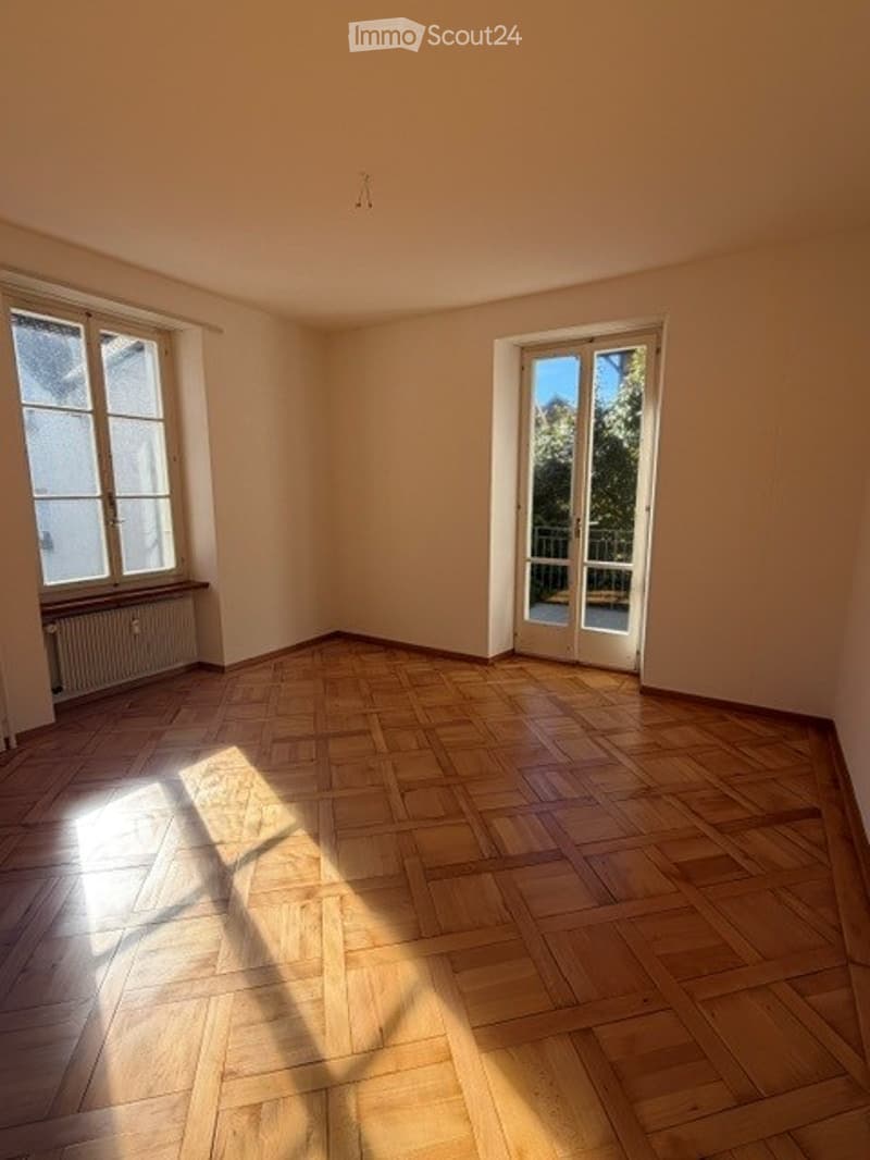 Empty room with wooden flooring, large windows, and a sliding glass door leading to a balcony.