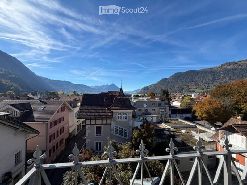 Balcony overlooking a town with traditional houses and surrounding mountains under a clear blue sky.