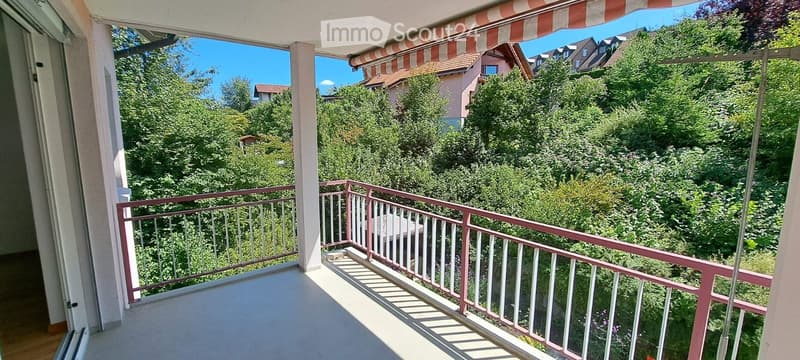 Balcony with a striped awning, metal railing, and a view of lush greenery and neighboring houses.