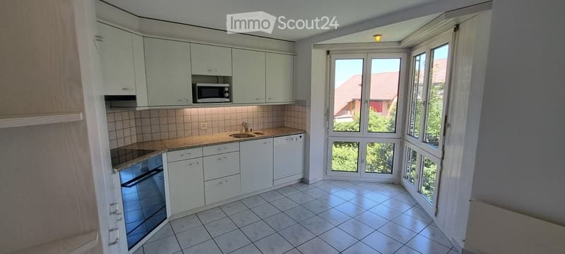 Modern kitchen with white cabinets, granite countertops, tiled floor, and large windows offering a view of the neighborhood.