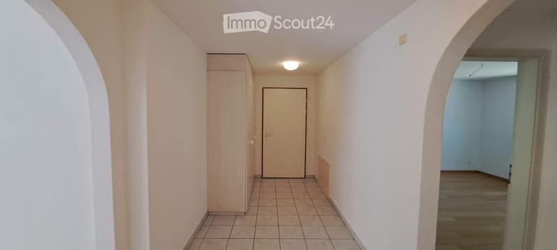 Empty hallway with tiled floor, white walls, and a closed door leading to another room.