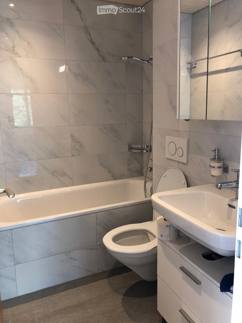 Modern bathroom with marble tiles, bathtub, toilet, sink, and mirror.