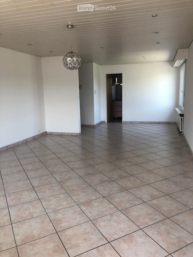Empty room with tiled floor and white walls, featuring a modern chandelier and a doorway leading to another room.