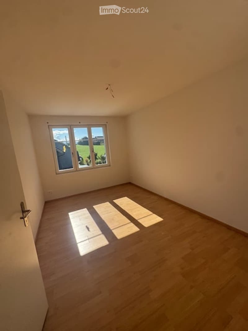 Empty room with wooden flooring and a large window showing a view of the outdoors.