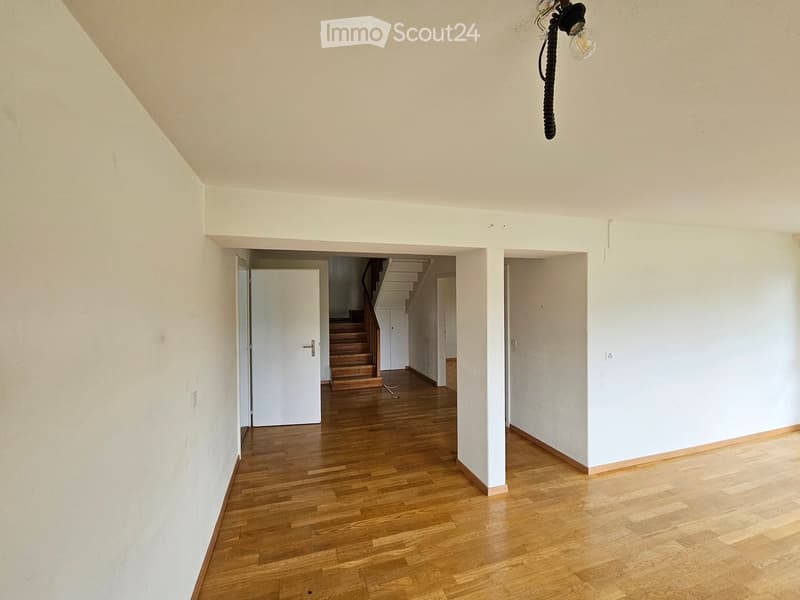 Empty room with wooden flooring, white walls, and a visible staircase leading upwards.